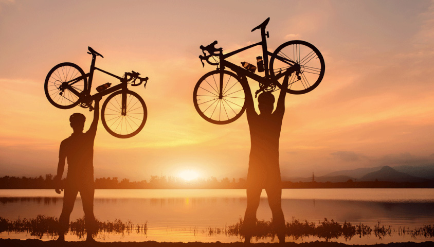 Bicycle riders with their bikes above head in the sunset